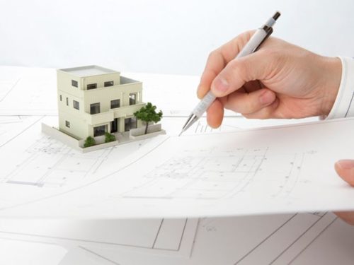 家の模型と設計図に加筆する男性